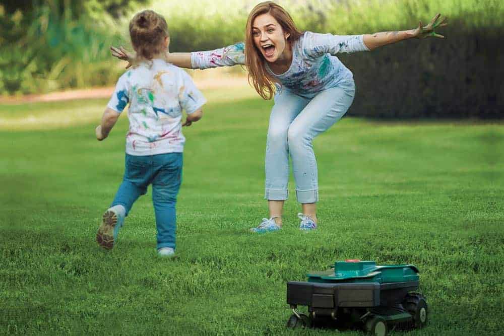 Girl playing with daughter while robotic mower mows